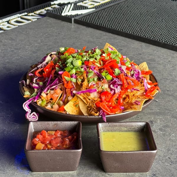 A large plate of colorful nachos with shredded chicken, red cabbage, peppers, and green onions, served with salsa and guacamole.