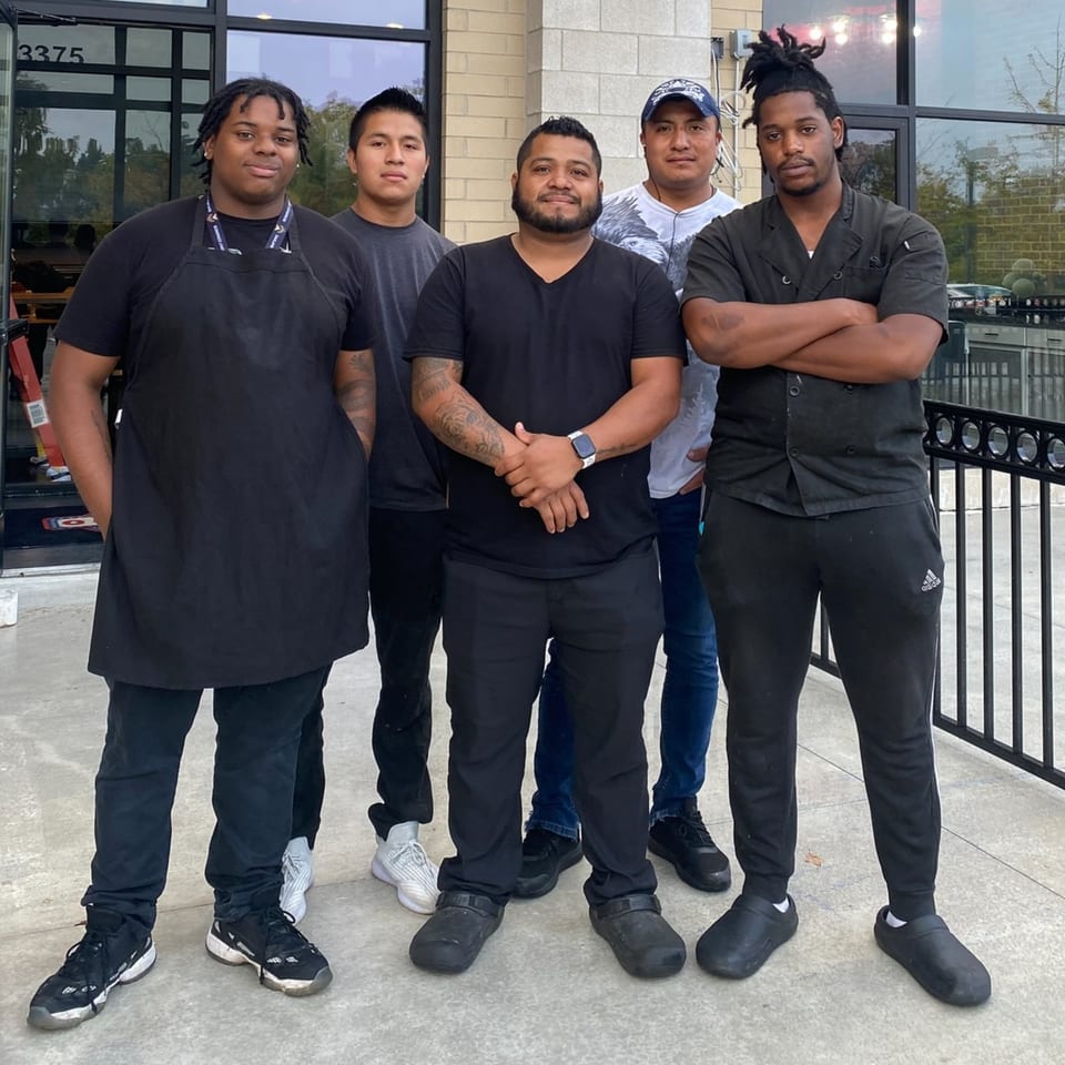 Five male O Grizzly's Bar & Bistro staff members stand outside the restaurant entrance.