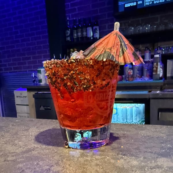 A vibrant red cocktail with a sugared rim and a small umbrella sits on a bar counter at O Grizzly's.