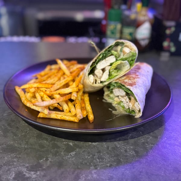 Chicken Caesar wrap with crispy fries on a dark plate at O Grizzly's Bar & Bistro.