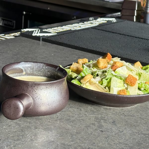 A bowl of creamy soup and a Caesar salad with croutons on a dark bar counter at O Grizzly's.