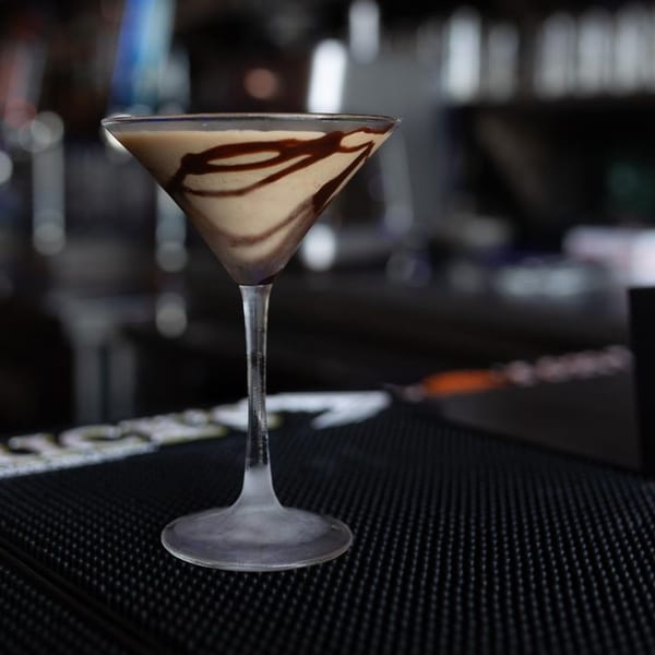 A chocolate martini with chocolate syrup swirls in a frosted glass on a bar mat.