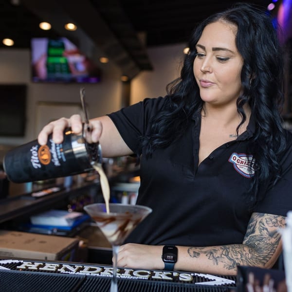 A bartender at O Grizzly's Bar & Bistro pours a creamy cocktail from a shaker into a martini glass.