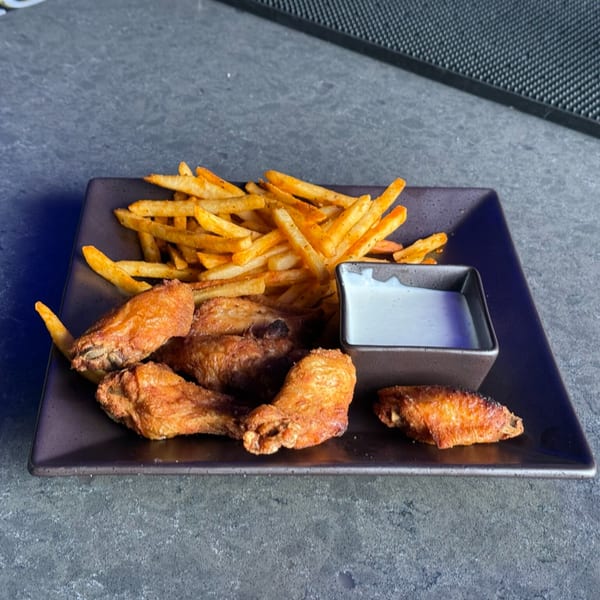 Crispy chicken wings, seasoned fries, and a side of dipping sauce on a dark plate at O Grizzly's.