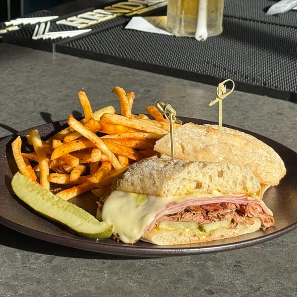 A Grizzly's Bar & Bistro Cuban sandwich with fries and a pickle spear on a dark plate.