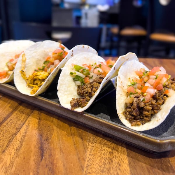Five tacos with various fillings and fresh pico de gallo on a dark serving tray.